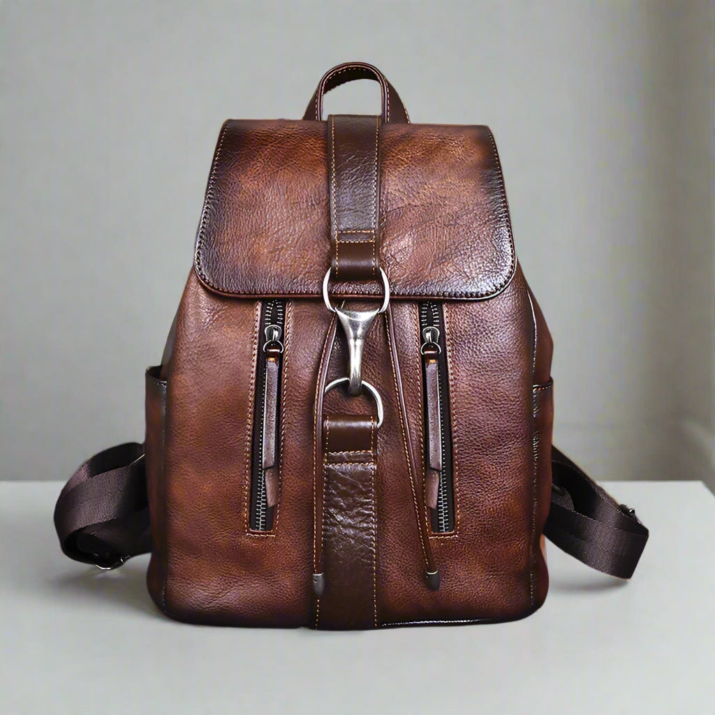 Brown leather backpack with multiple zippers on a white table