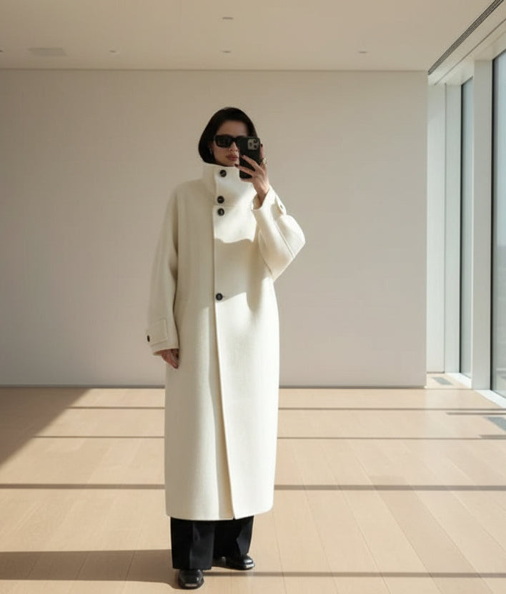 Person wearing a long white coat in a minimalistic room.