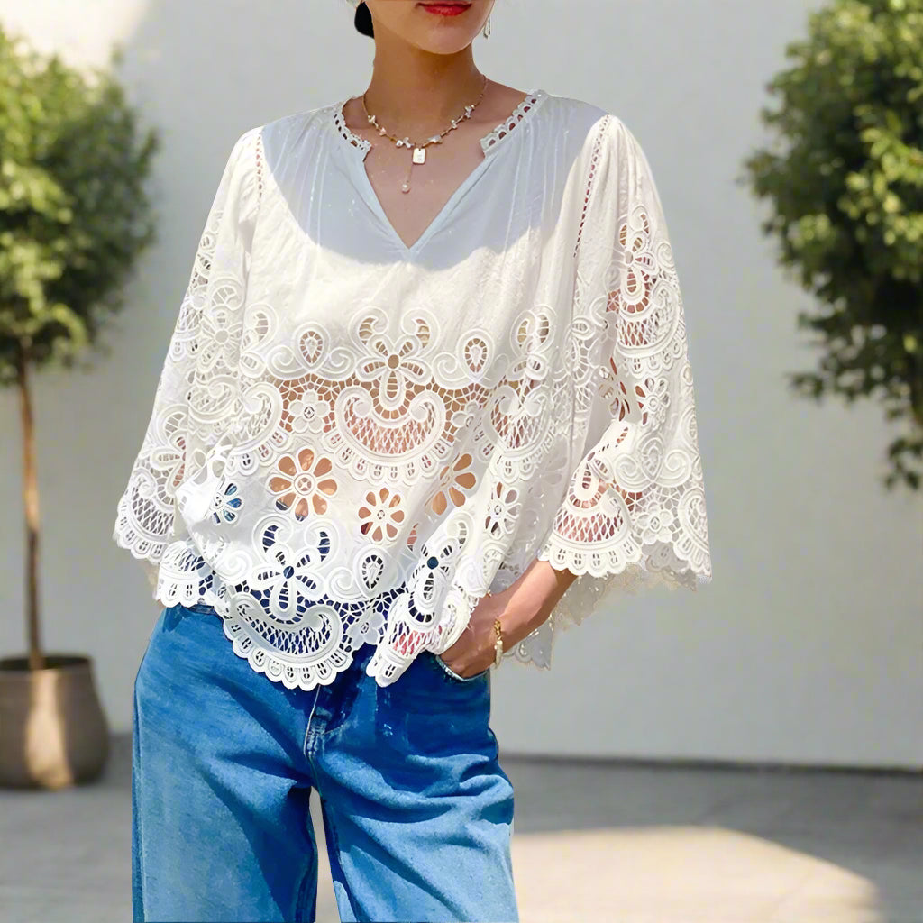 Person wearing a white lace top and blue jeans outdoors.