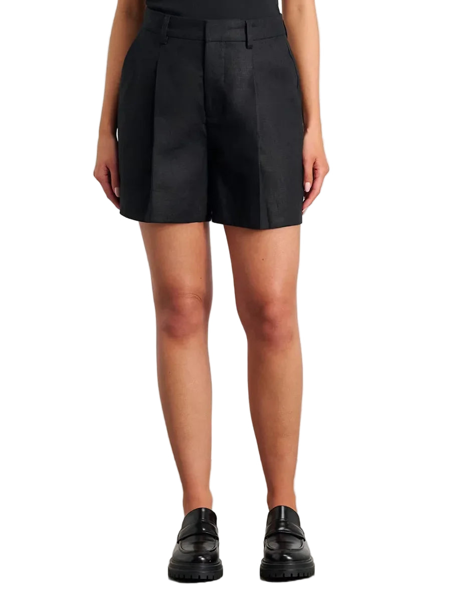 Person wearing a black pleated skirt with black shoes on a plain background