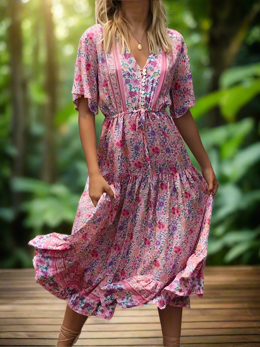 Woman wearing a pink floral dress standing outdoors with greenery in the background
