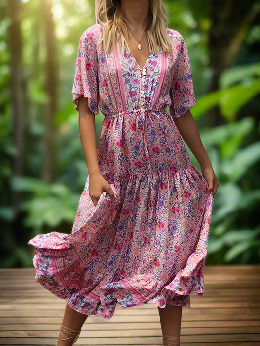 Woman wearing a pink floral dress standing outdoors with greenery in the background