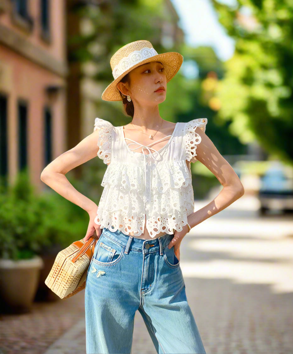 Woman wearing a white lace top and blue jeans, standing against a backyard garden, sunny