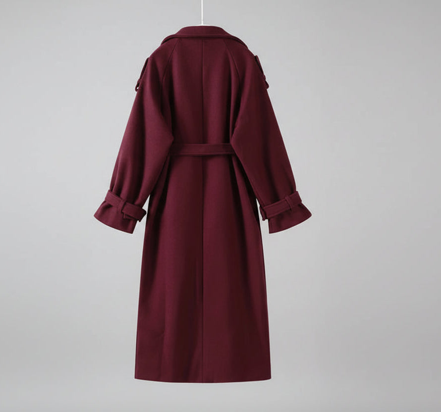 Maroon trench coat hanging against a white wall