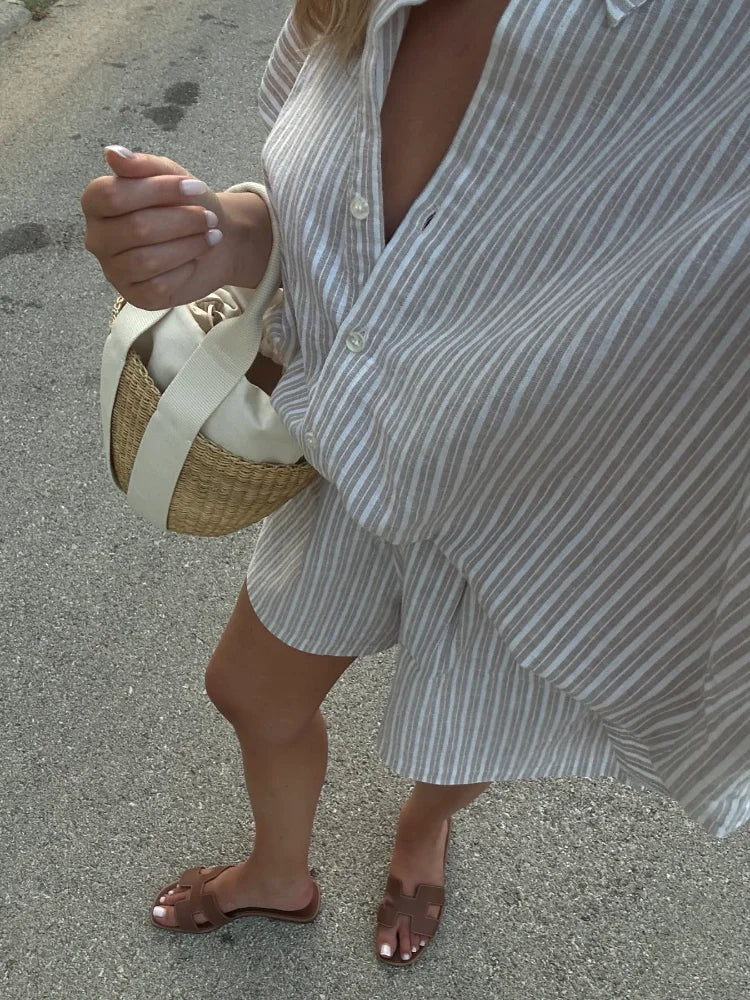Person wearing a white and gray striped dress holding a straw bag on a street.
