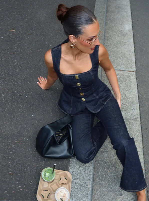 Woman in a dark blue outfit sitting on a street with a black bag and food containers.