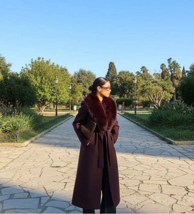 Woman in a long dark coat standing in front of an open park
