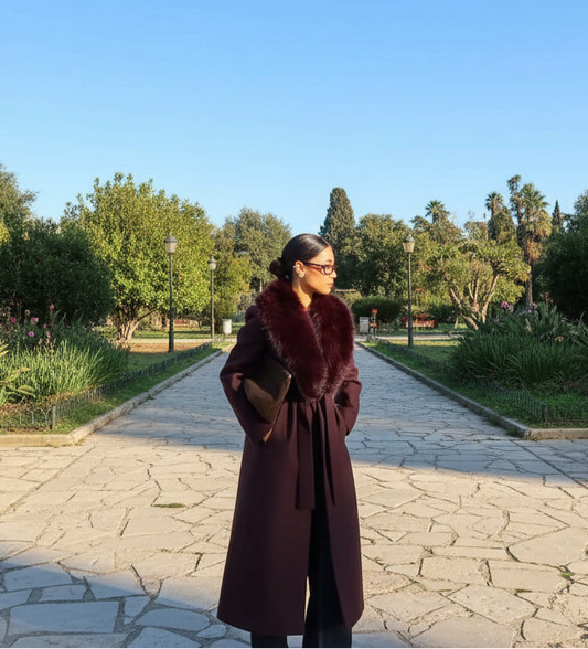 Woman in a long dark coat standing in front of an open park