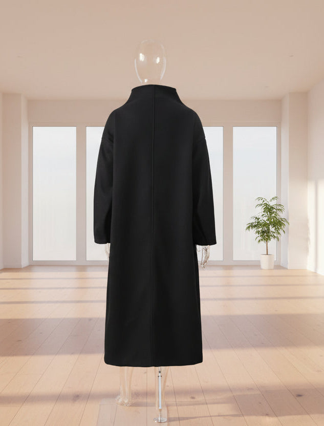 Black coat on a mannequin against a white wall with a plant in the corner