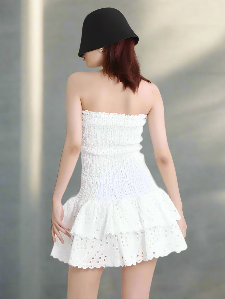 Woman wearing a white strapless dress with black hat on a plain background