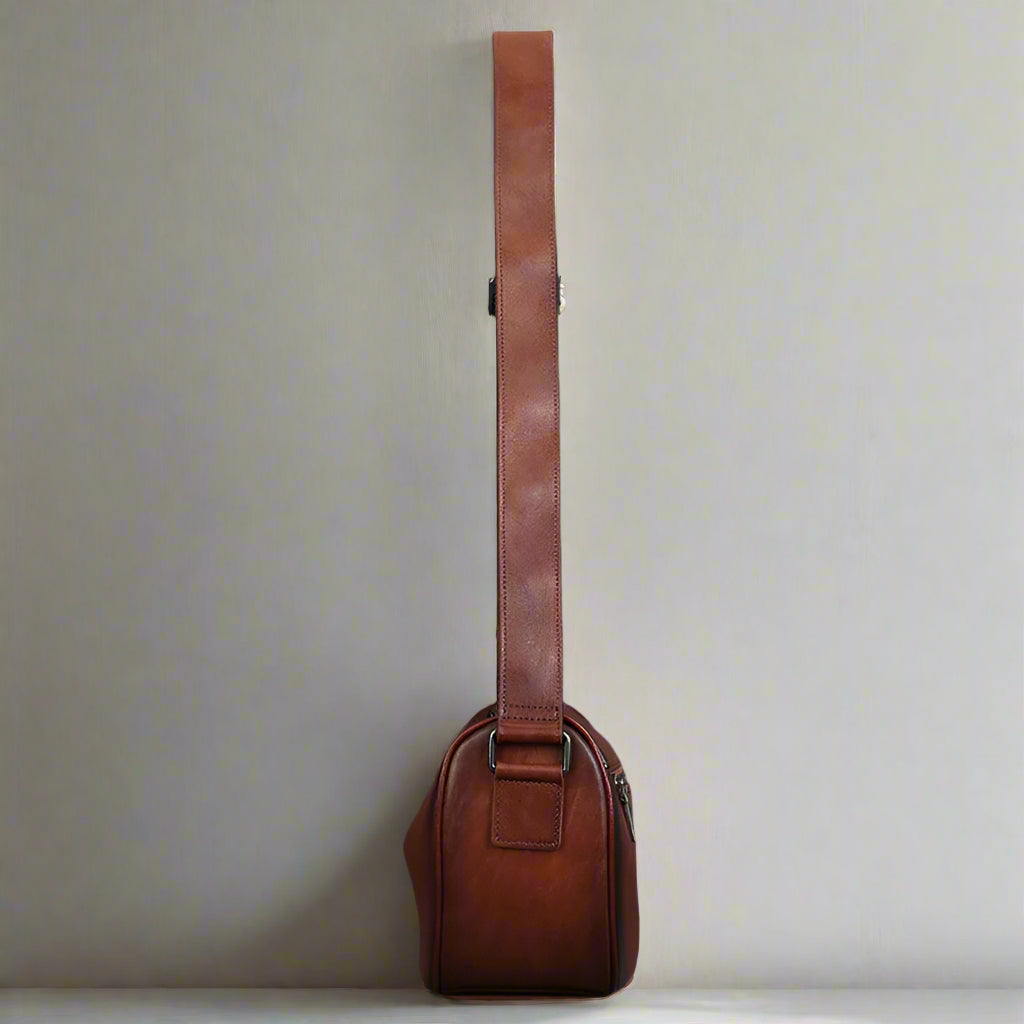 Brown leather guitar case with strap against a gray background