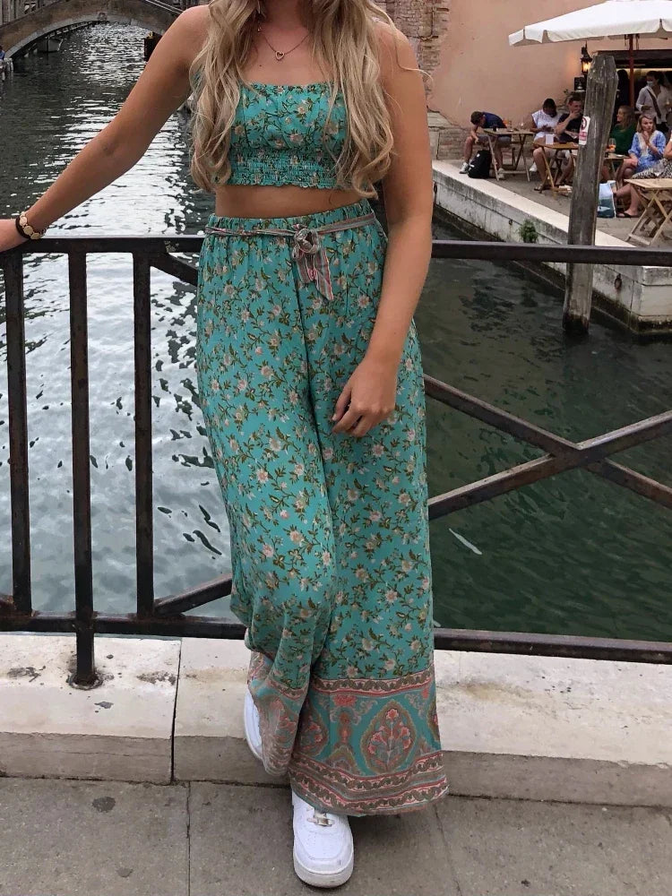 Woman in teal patterned outfit standing by a canal with a bridge and people in the background.