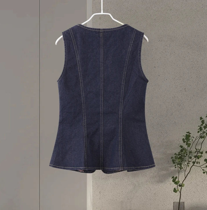 Denim sleeveless top on a hanger against a neutral wall with a plant in the corner.
