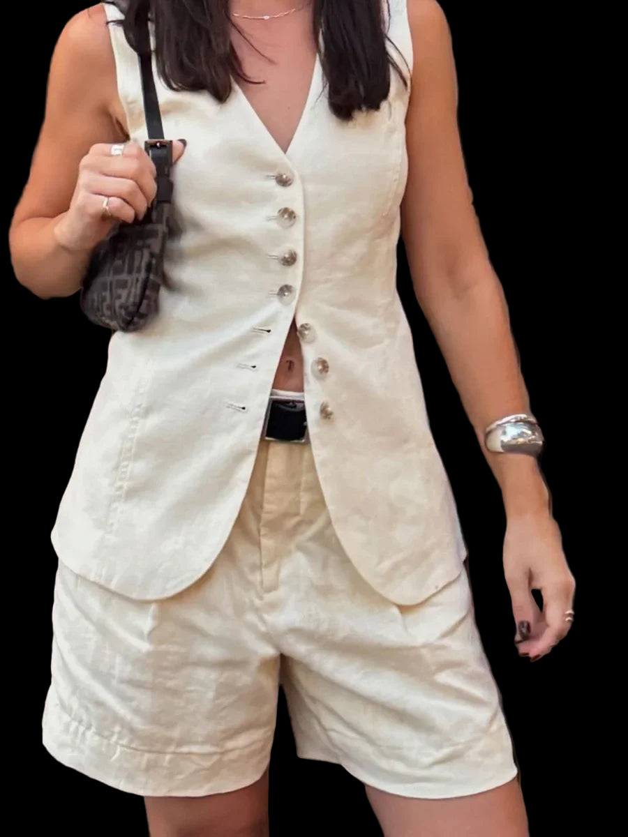 Person wearing a white sleeveless blazer and beige shorts against a black background